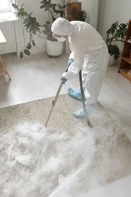 Close-up image of a yellow canister vacuum cleaner with a hose and wand attachment cleaning a patterned area rug on a wooden floor in a living room. In the background, there's a modern wooden TV stand